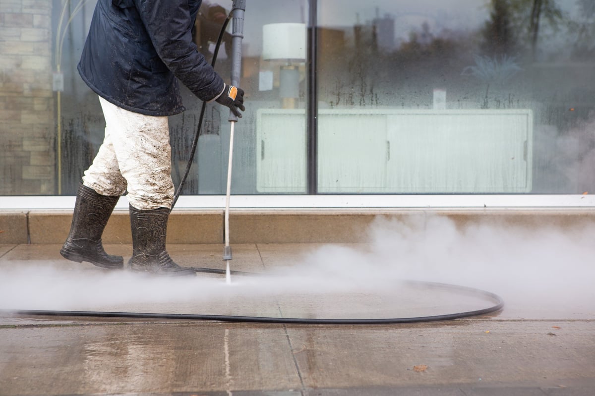 A worker power washing a sidewalk in rubber boots