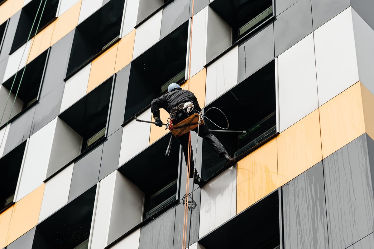 A window cleaner working at height washing windows with pressure equipment