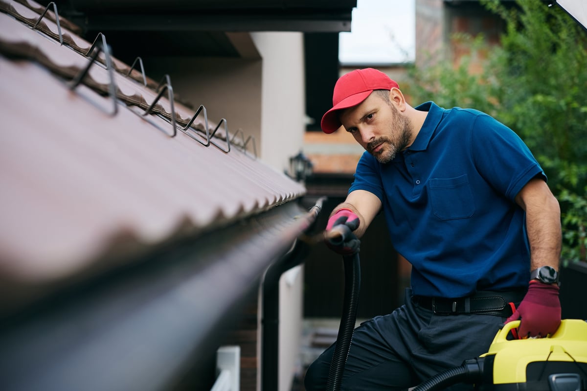A technician cleaning roof gutters to prevent clogs and water damage in autumn